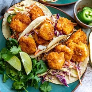 Baja shrimp tacos on a green plate with limes on the side.