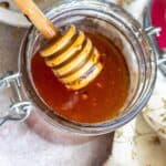 A jar full of honey with a honey stick.