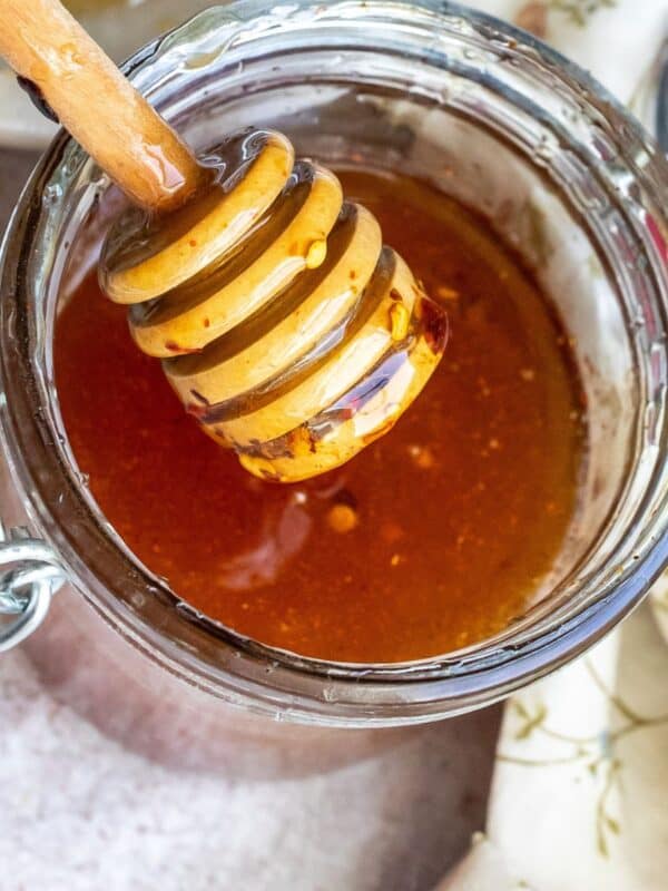 A jar full of honey with a honey stick.