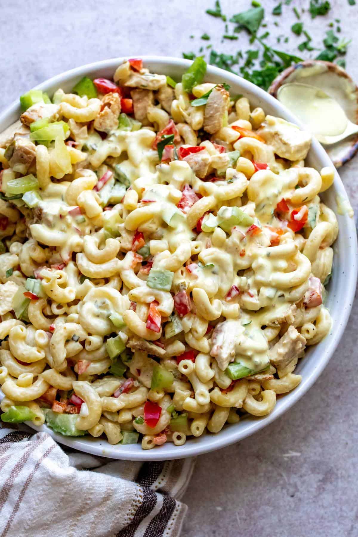 White ceramic bowl filled with chicken Macaroni pasta salad and a spoon with dressing to the side. 