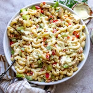 White ceramic bowl filled with chicken Macaroni pasta salad and a spoon with dressing to the side.