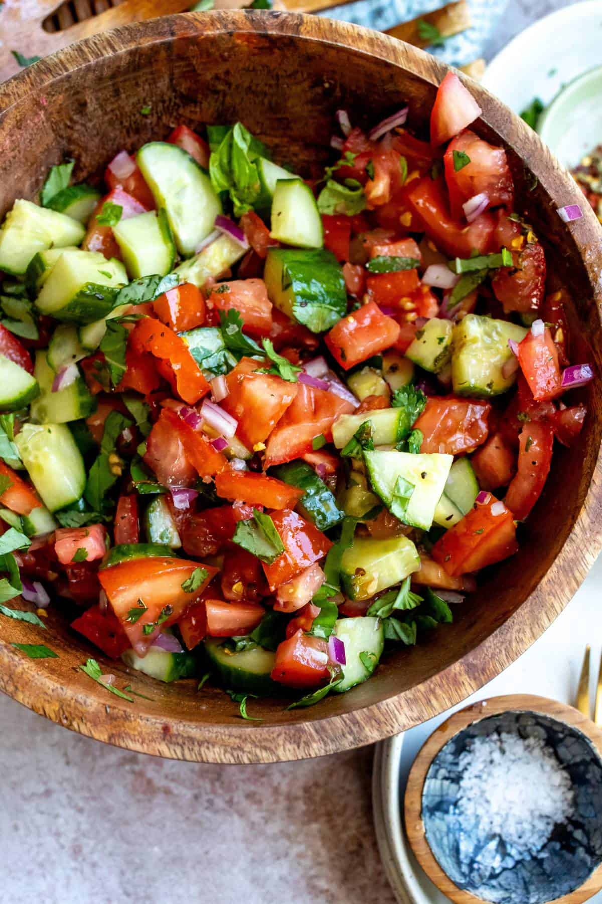 Wooden bowl with tomatoes and cucumber in it, red pepper flakes on the side.