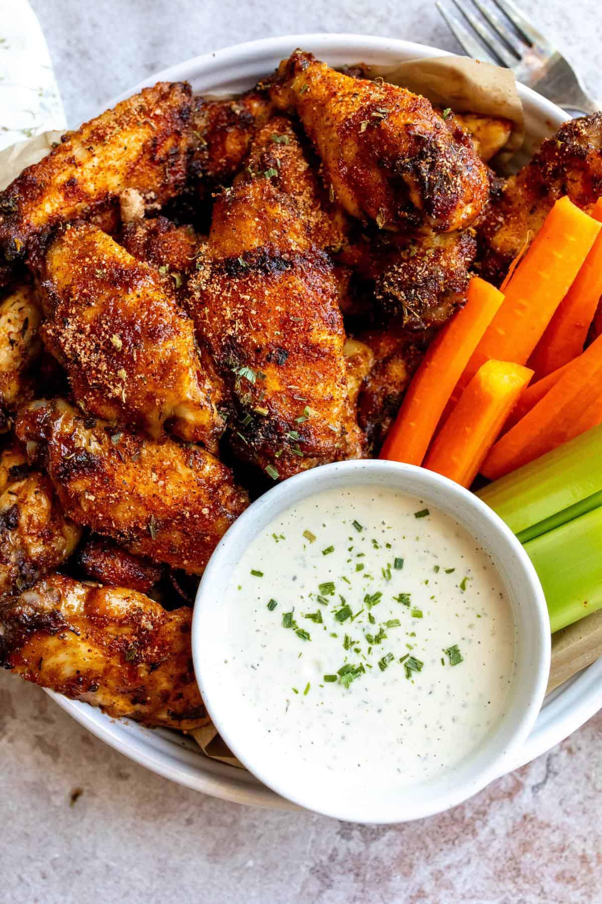 An overhead image of dry rub wings with a dipping sauce, carrot sticks and celery on the side.