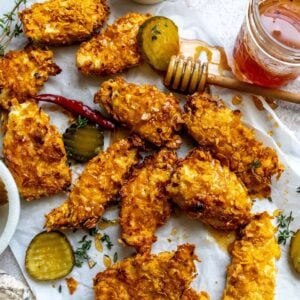 Hot honey chicken tenders on parchment paper with pickles on the side.