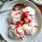 An overhead image of four scoops of strawberry cheesecake ice cream in a bowl with a spoon resting on the side.