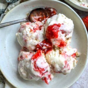 An overhead image of four scoops of strawberry cheesecake ice cream in a bowl with a spoon resting on the side.