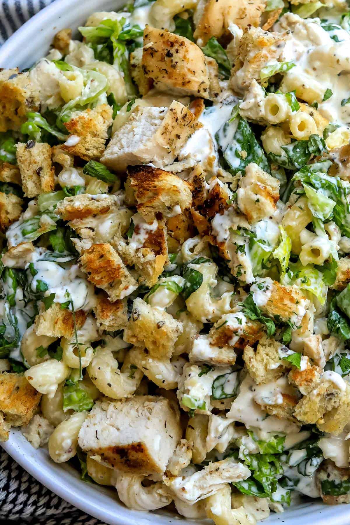 White ceramic bowl with Chicken Caesar Pasta Salad and utensils to the side.  Up close photo. 