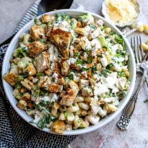 White ceramic bowl with Chicken Caesar Pasta Salad and utensils to the side.