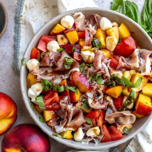 Grey bowl with peach and tomato in it, two plates on the side.