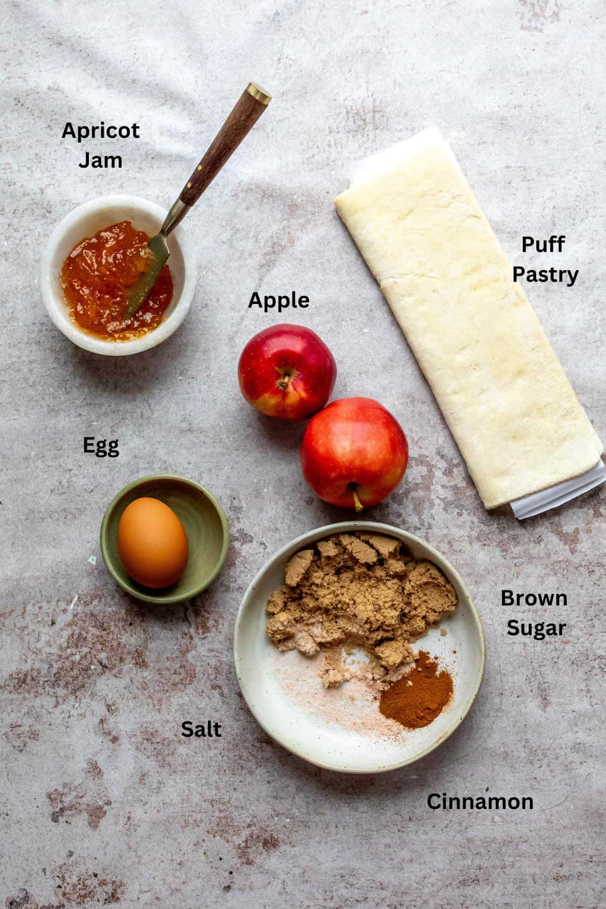 An image of apples, butter, puff pastry, jam, spices, and an egg.