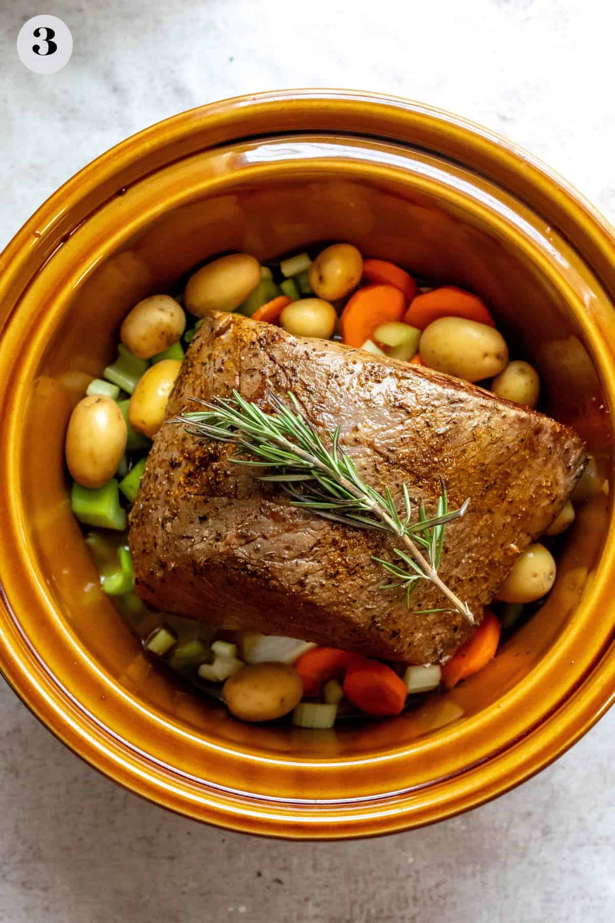 An image of cooking beef with carrots and potatoes in a slow cooker.