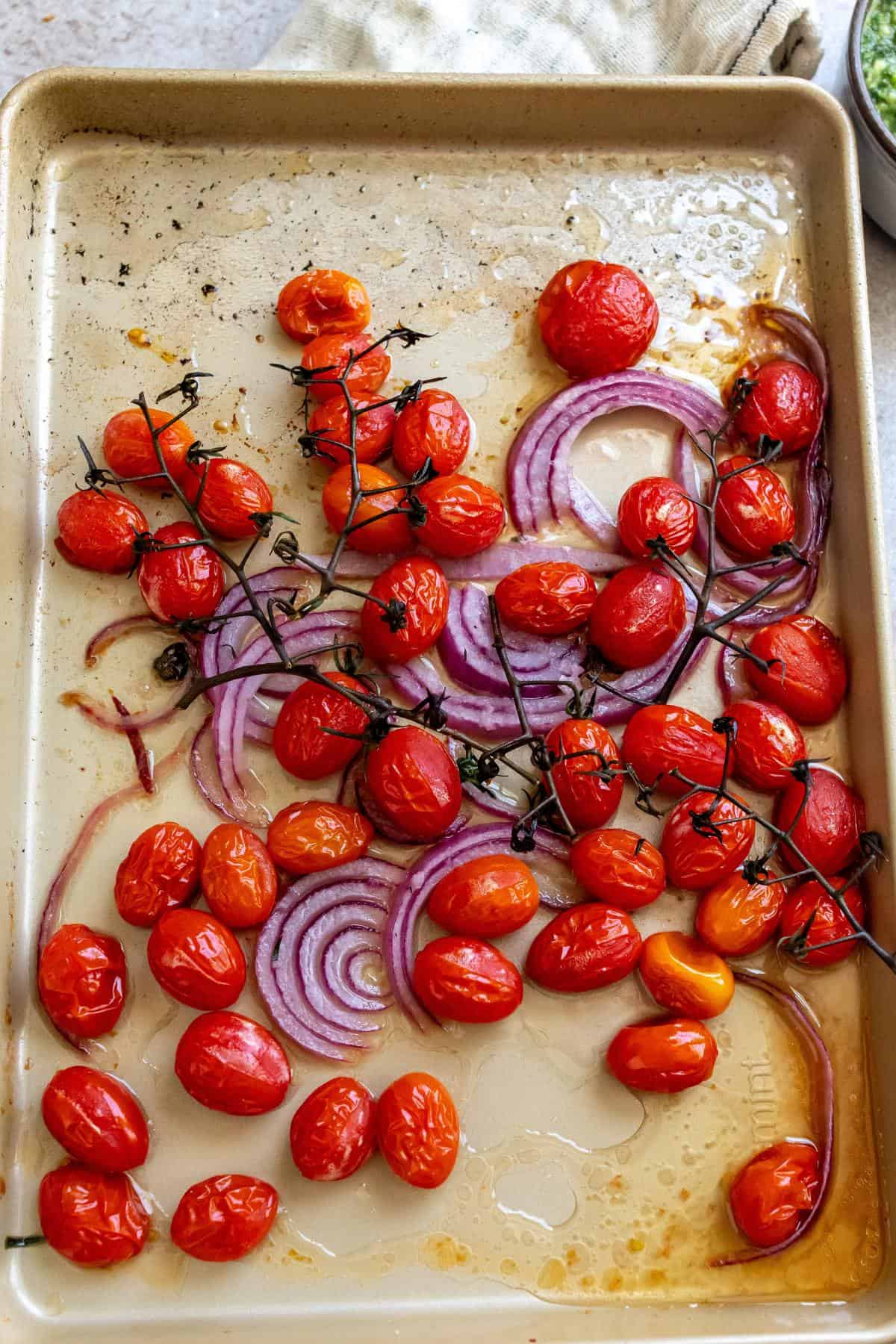 Sheet pan with roasted tomatoes and onions on it. 