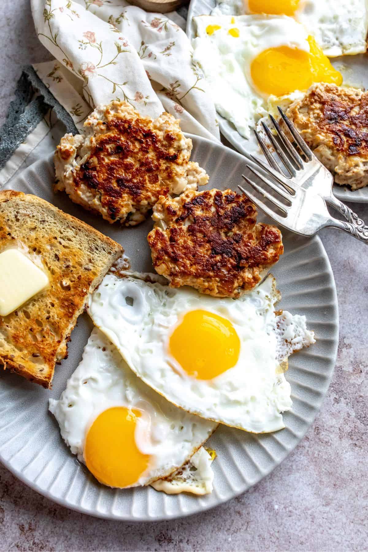 An image of chicken apple sausages with two fried eggs and a toasted bread on a plate.