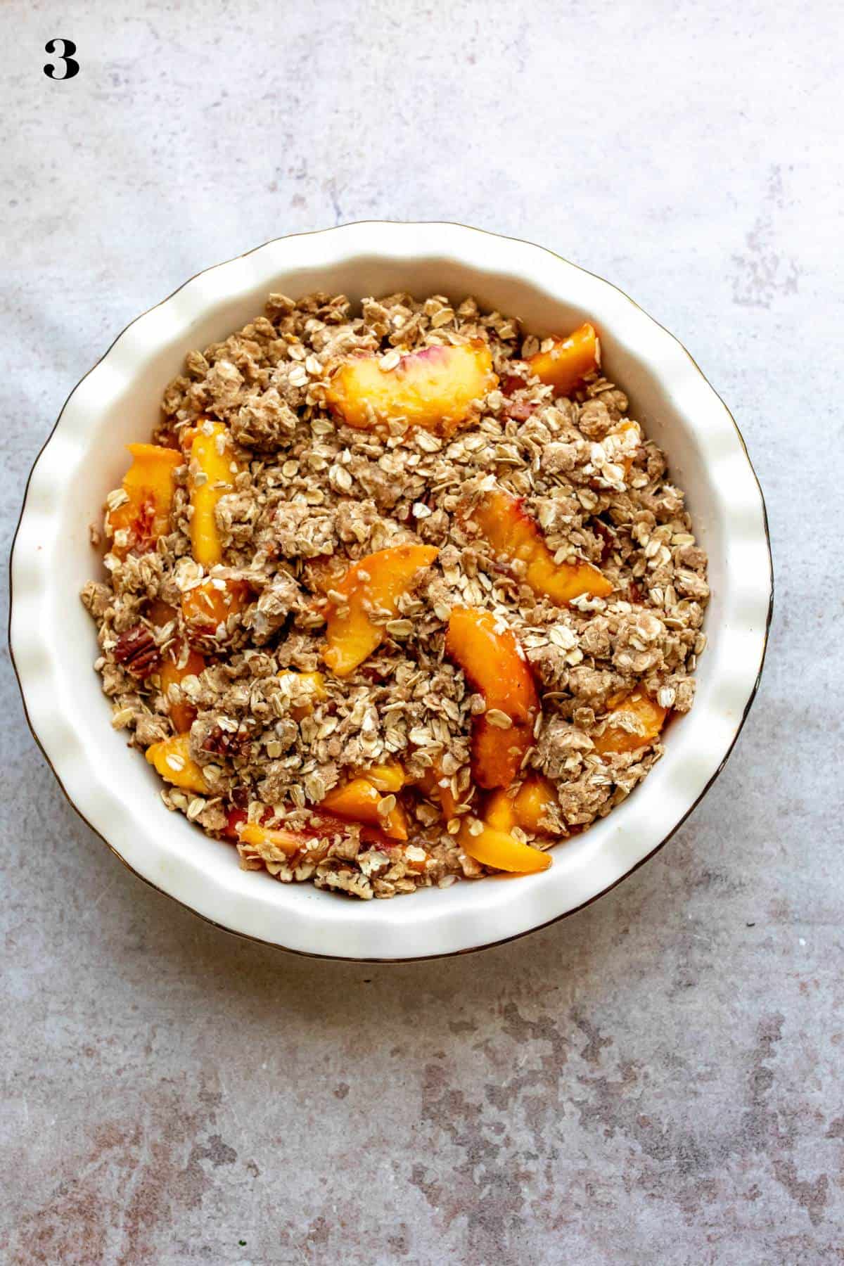 White ceramic bowl with peaches  and crumble in it. 