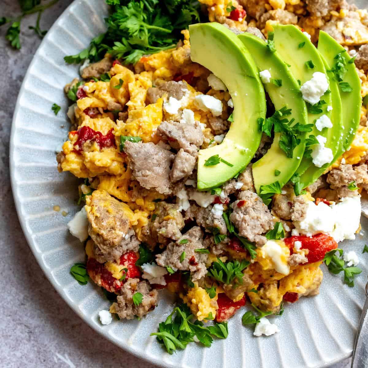 An image of turkey sausage on a plate with eggs, avocados, and veggies.