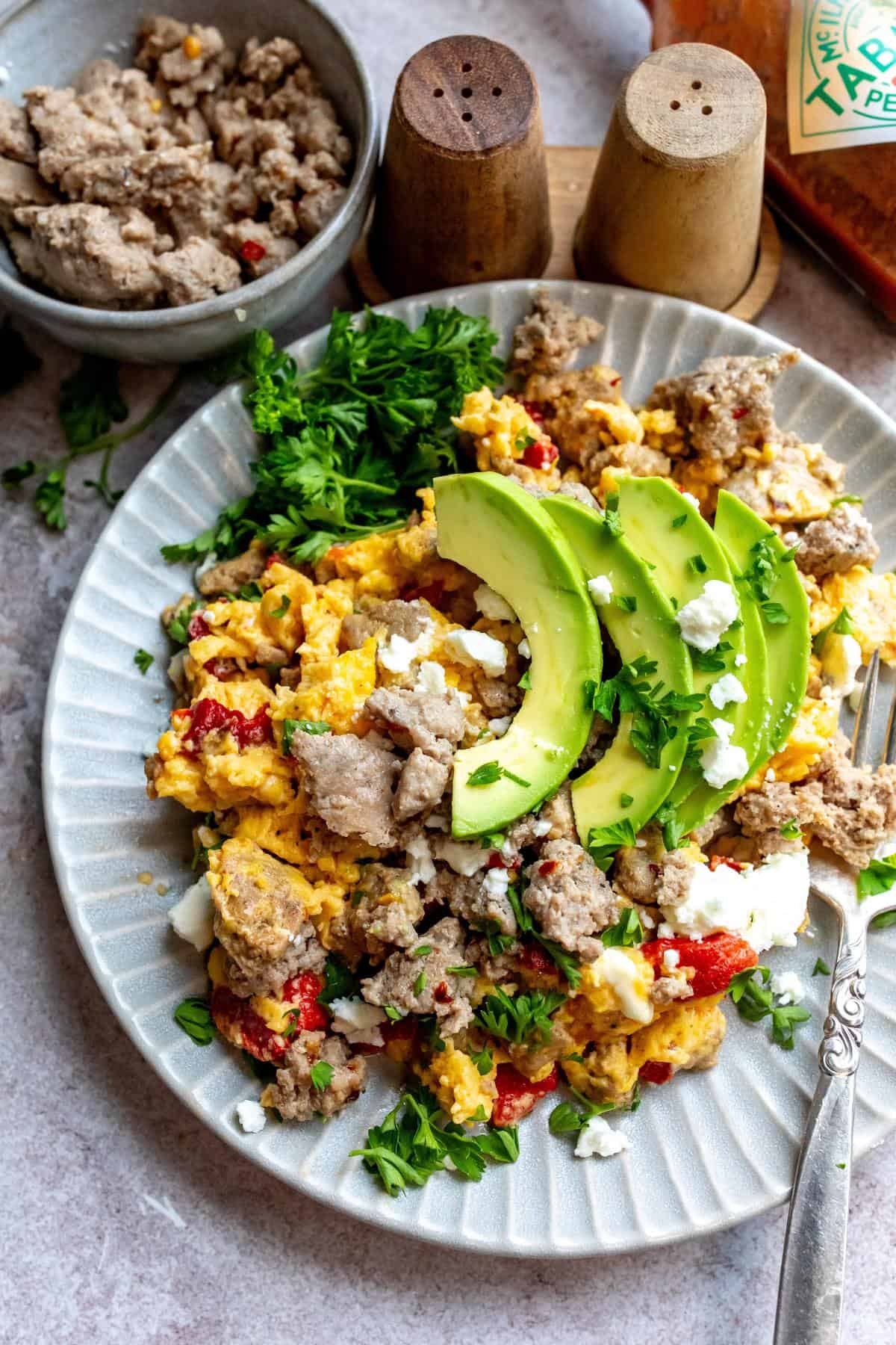 An image of turkey sausage on a plate with eggs, avocados, and veggies.