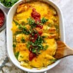 White casserole dish with Breakfast Enchiladas in it and wooden spatula.