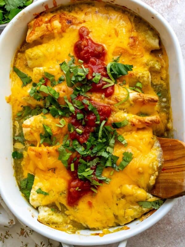 White casserole dish with Breakfast Enchiladas in it and wooden spatula.