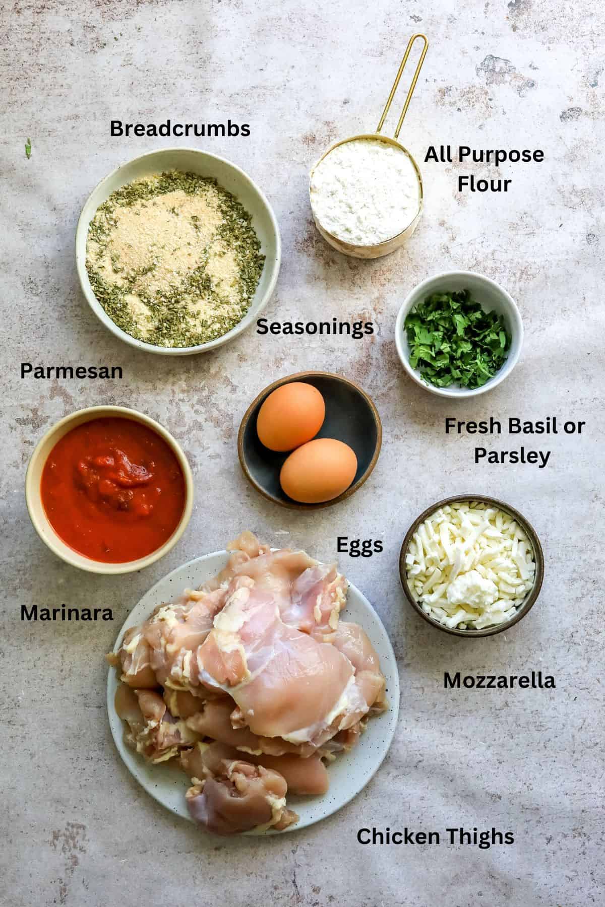 Ingredients to make chicken parmesan on a counter in small bowls and measuring cups. 