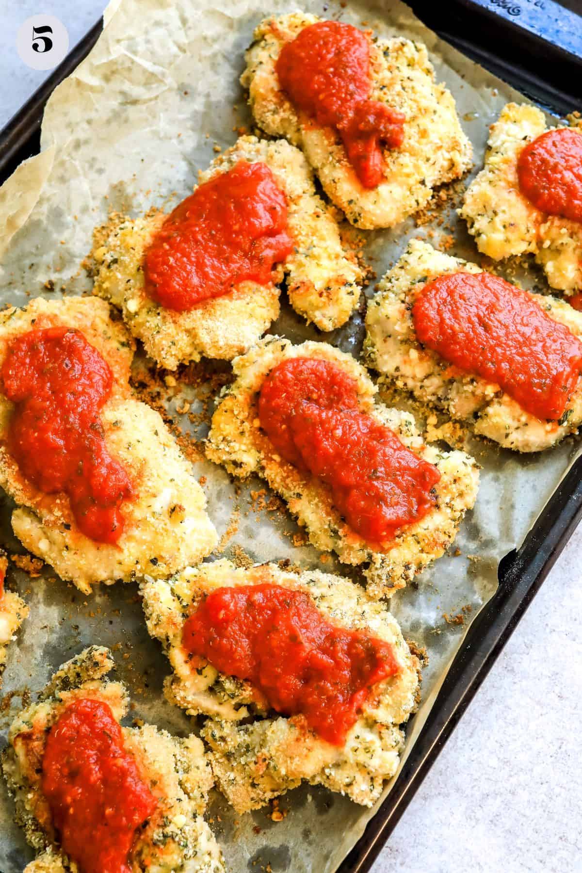 Breaded chicken on a baking sheet with marinara on top. 