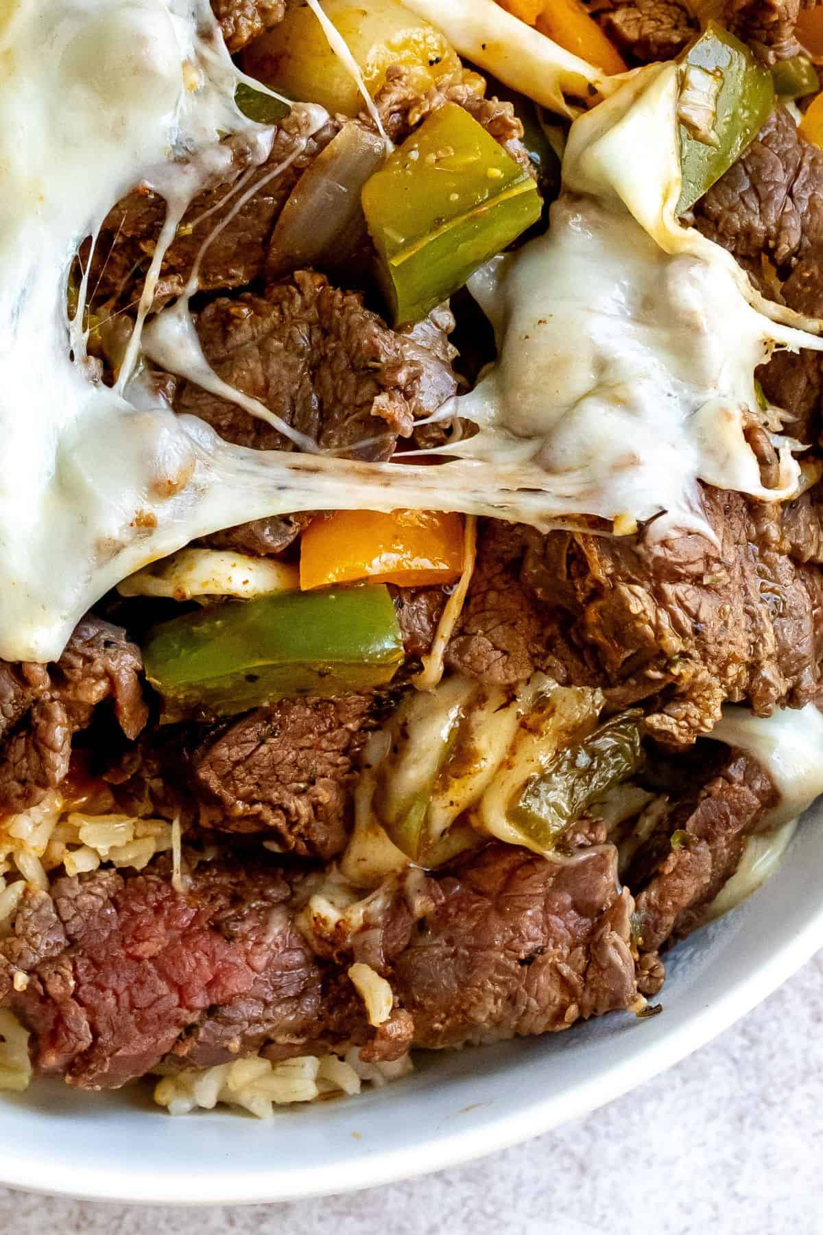 Up close photo of steak with cheese and peppers in a white bowl. 