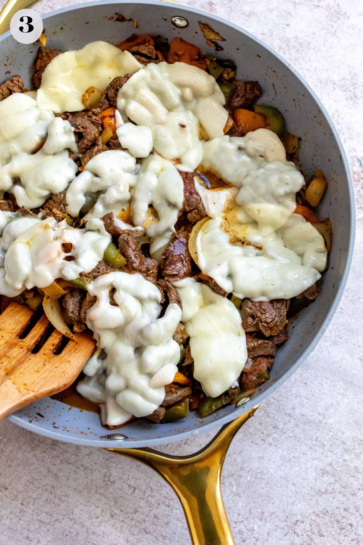 Grey skillet with gold. Filled with peppers and steak and melted cheese over the top.