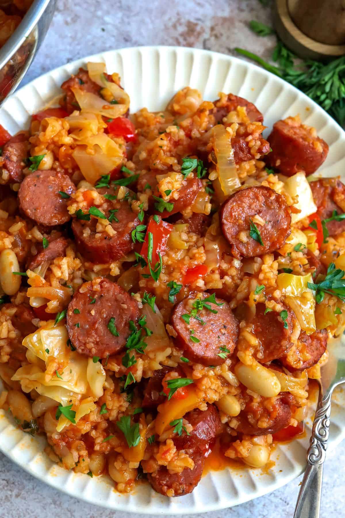 White plate with slow cooker sausage casserole on it and a fork to the side up close. 