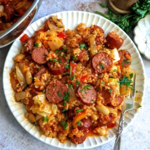 White plate with slow cooker sausage casserole on it and a fork to the side.