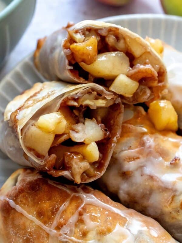 Crispy apple pie egg rolls on a plate with icing.