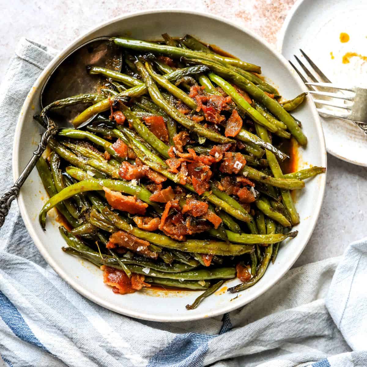 An overhead image of crack green beans on a plate, with bacon bits on top.