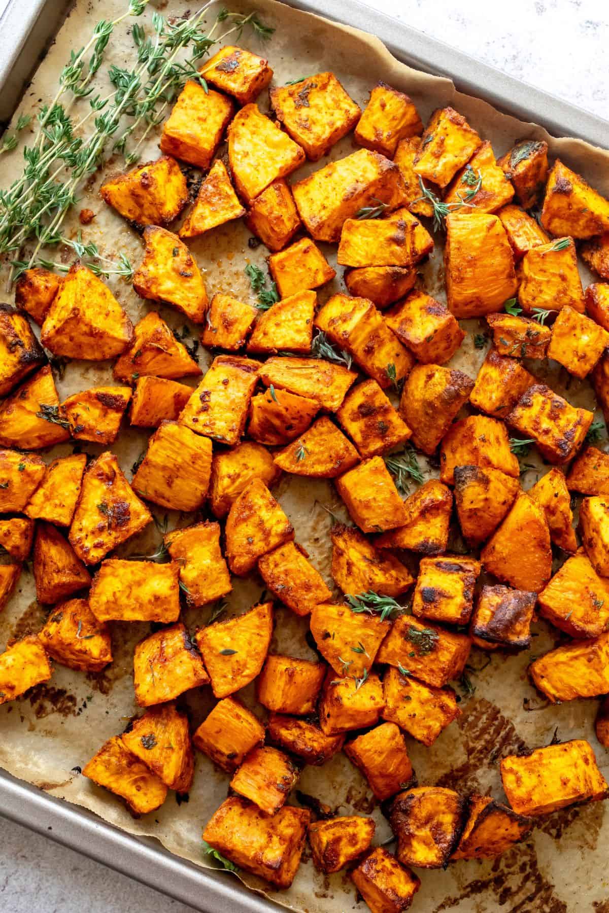 Parchment lined baking sheet with Crispy Roasted Sweet Potatoes and fresh thyme.