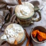 An overhead image of two cups of pumpkin chai latte garnished with cinnamon sticks.
