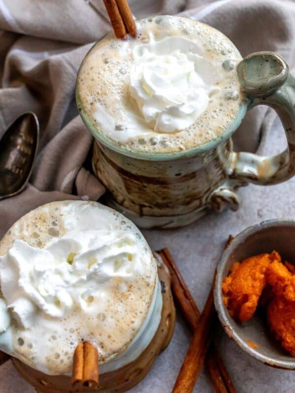 An overhead image of two cups of pumpkin chai latte garnished with cinnamon sticks.