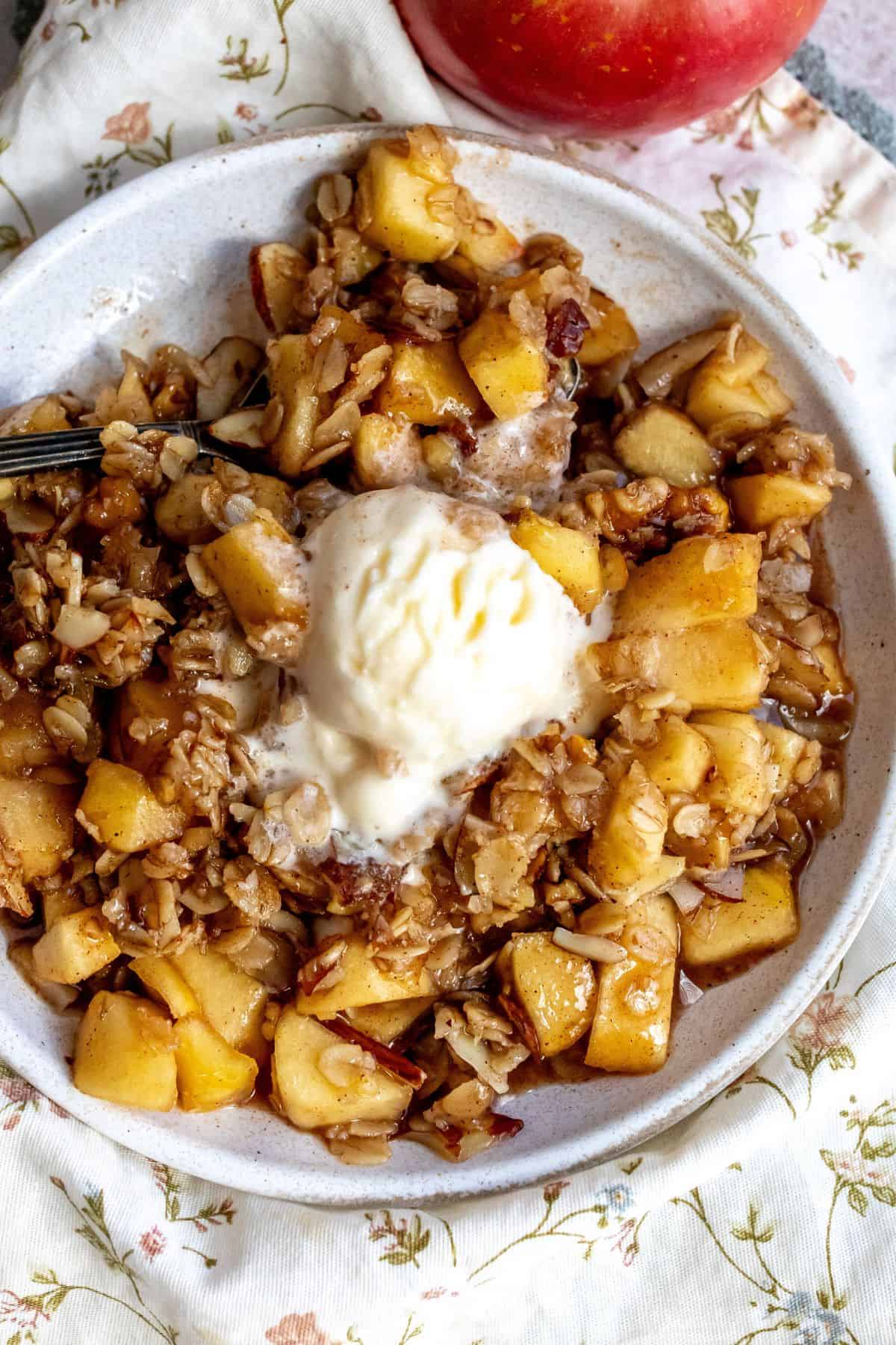 Up close photo of apple crisp with ice cream on top and a silver fork. 