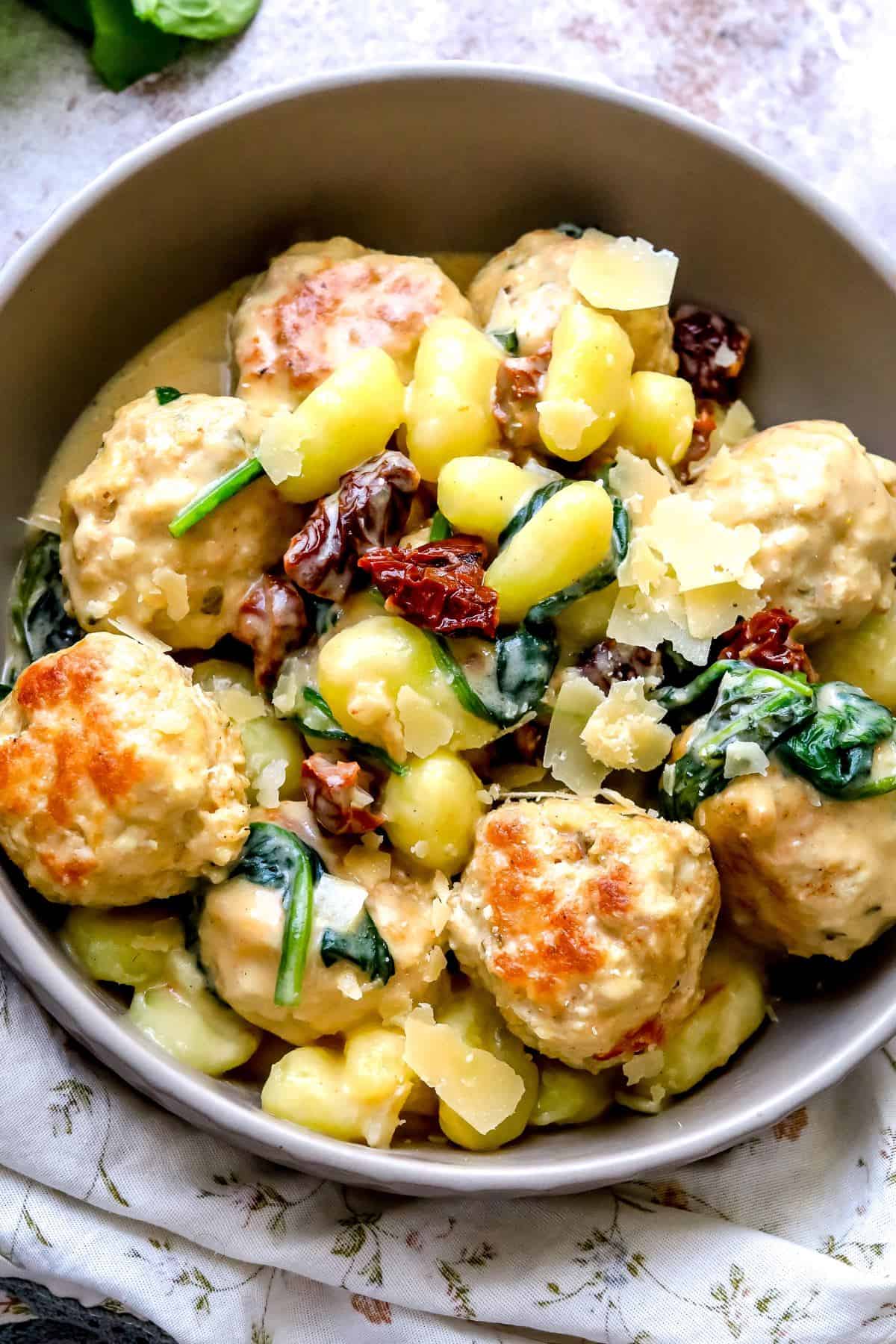 Grey bowl with Slow Cooker Tuscan Chicken Meatballs with Gnocchi in it. Parmesan on top. 