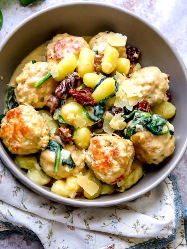 Grey bowl with Slow Cooker Tuscan Chicken Meatballs with Gnocchi in it. Parmesan on top.