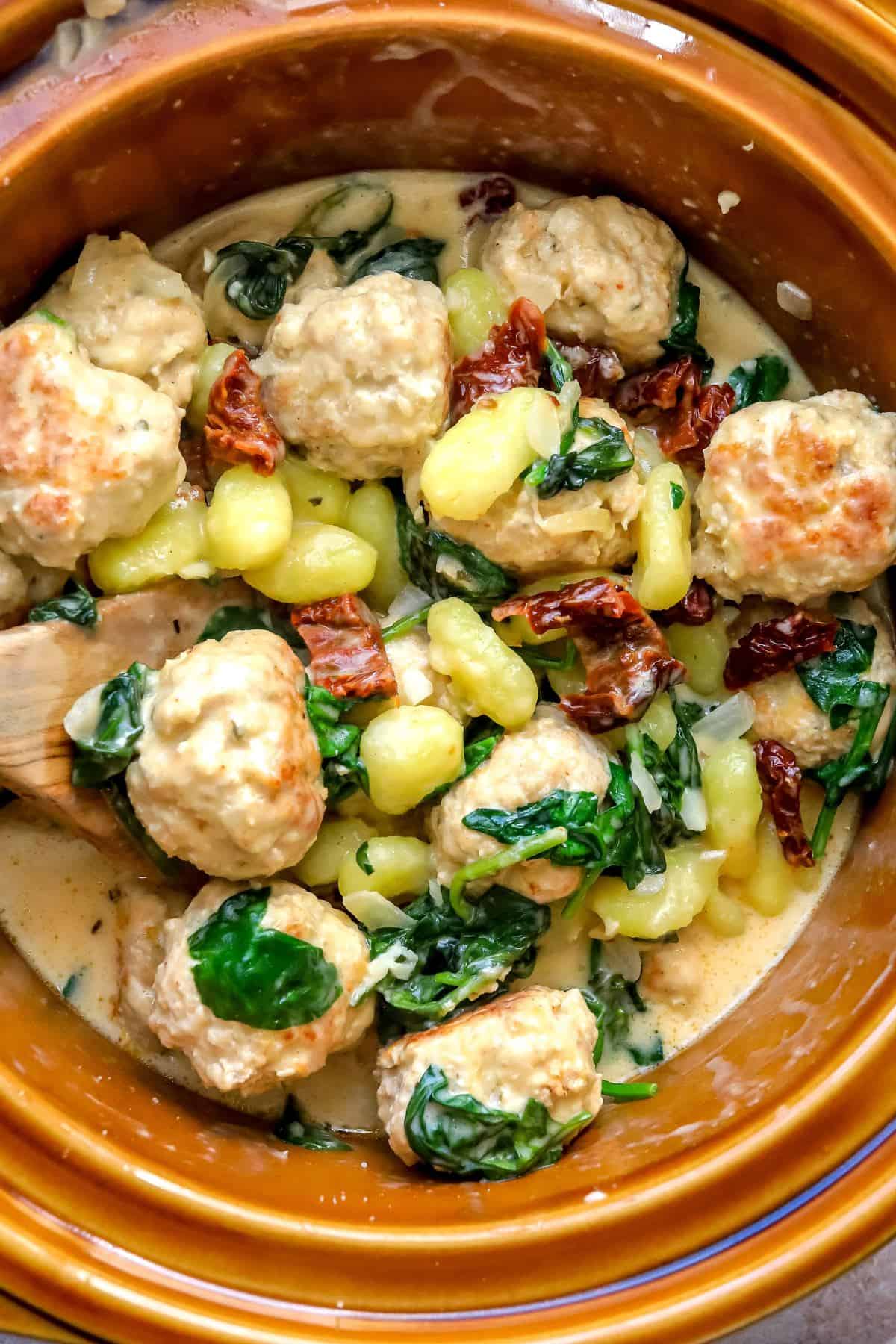 Brown crockpot with Slow Cooker Tuscan Chicken Meatballs with Gnocchi in it up close. 