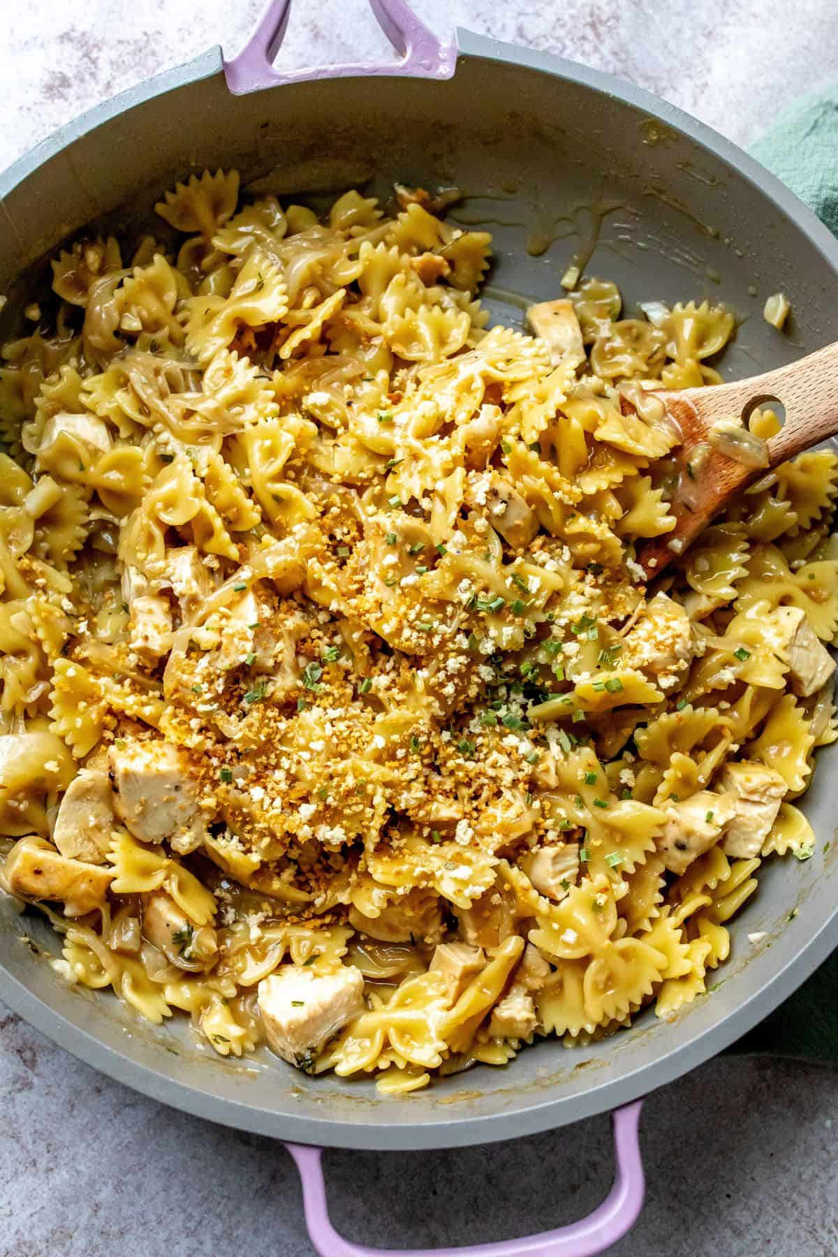 Grey and ink skillet with French Onion Pasta in it and a wooden spoon. 