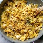 Grey and pink skillet with French Onion Pasta in it and a wooden spoon.