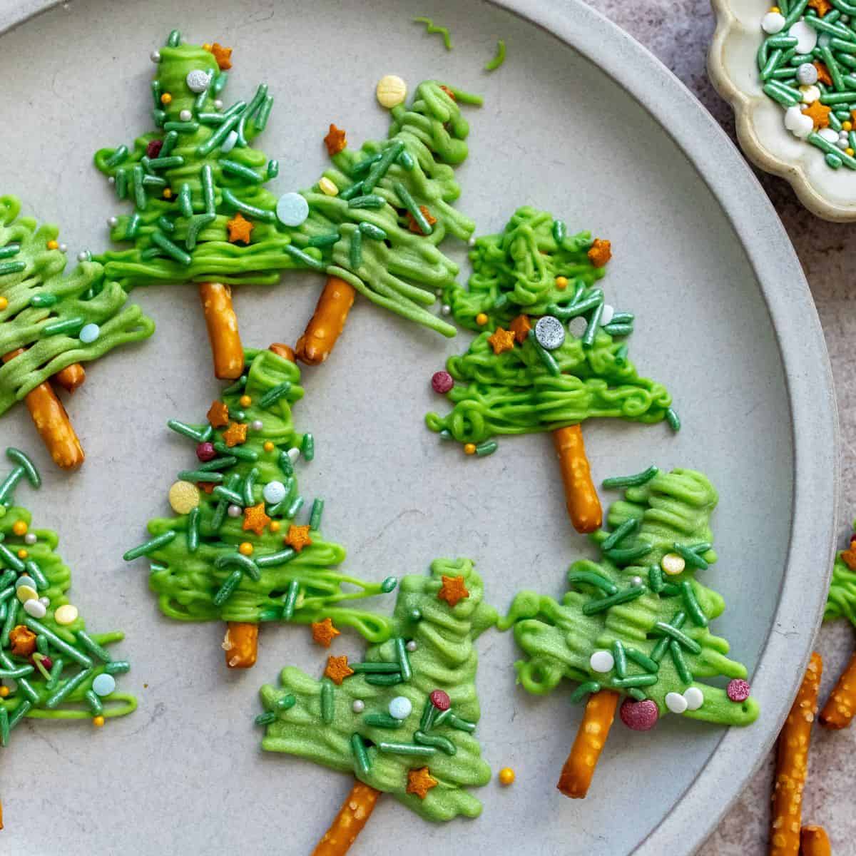 White plate with Pretzel Christmas Trees on it and sprinkles on the side.