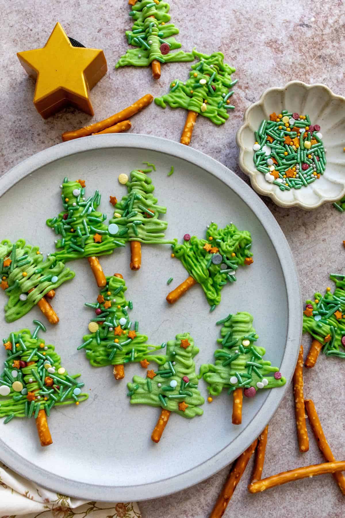 White plate with  Pretzel Christmas Trees on it and sprinkles on the side. 