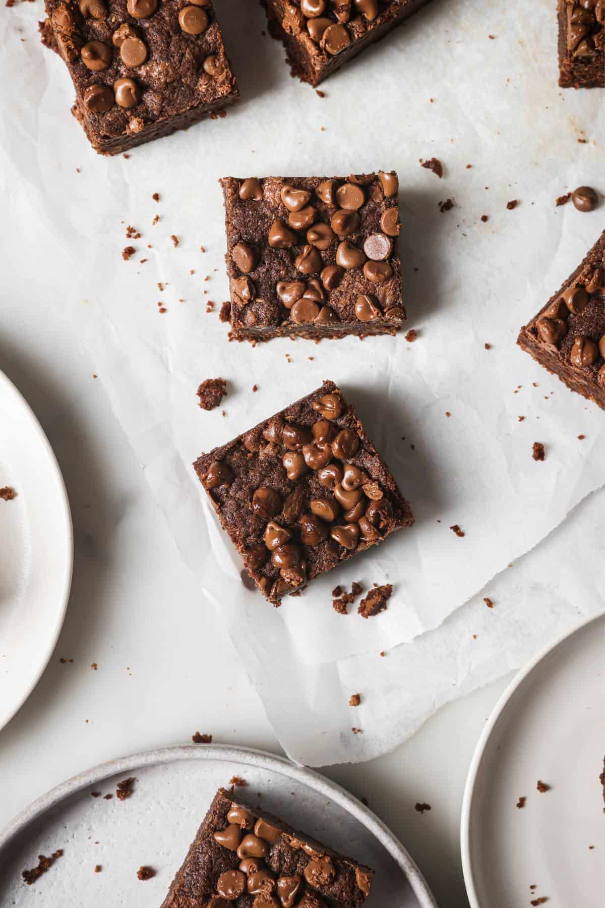 Chocolate Chocolate Chip Cookie Bars on white parchment paper with plates to the side.