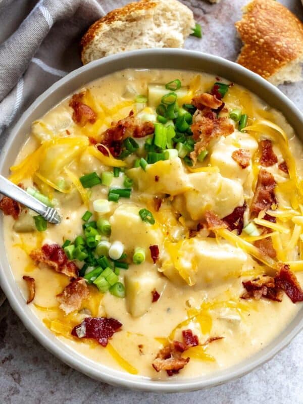 Grey ceramic bowl with Loaded Potato Soup in it and lots of cheese. and bread on the side.