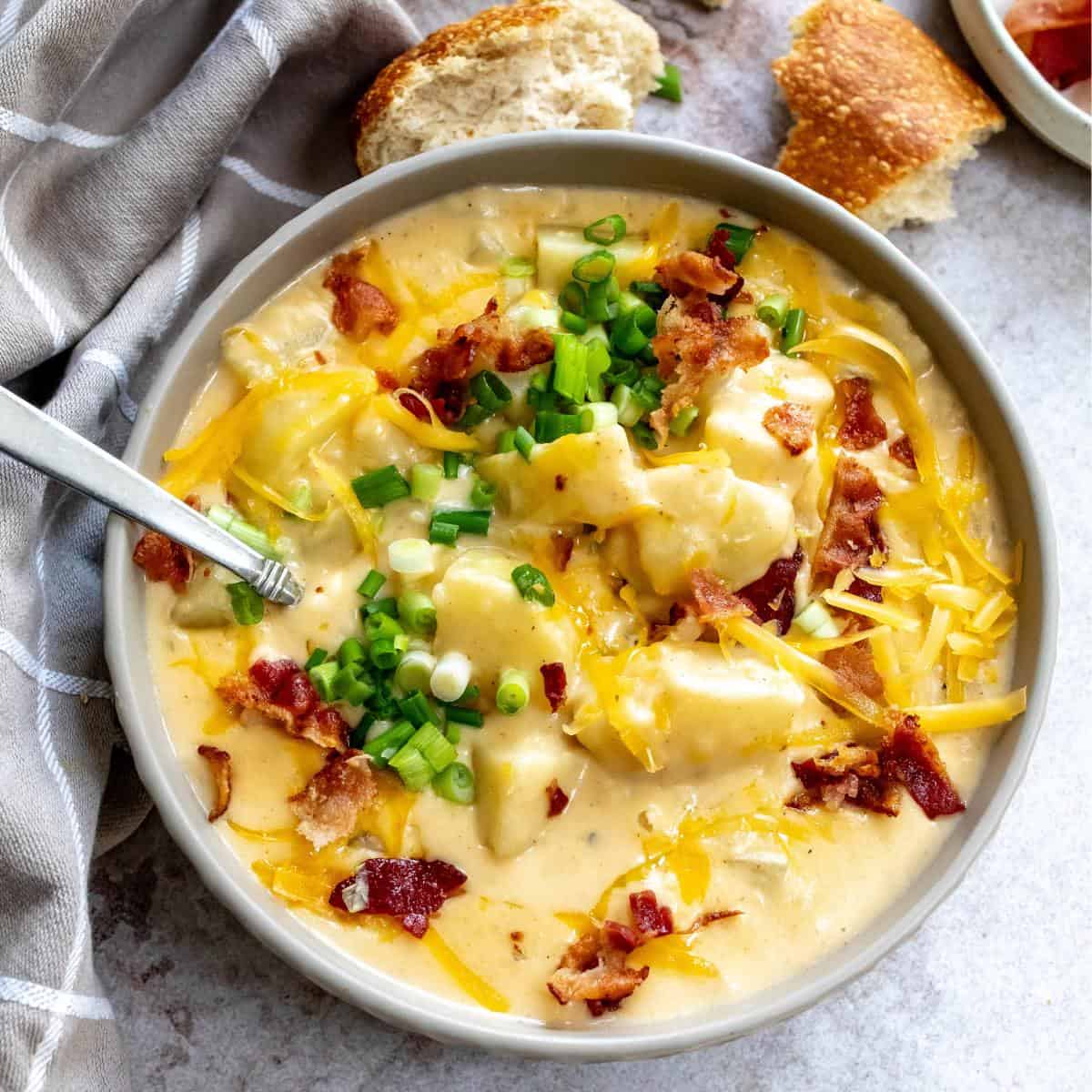 Grey ceramic bowl with Loaded Potato Soup in it and lots of cheese. and bread on the side.