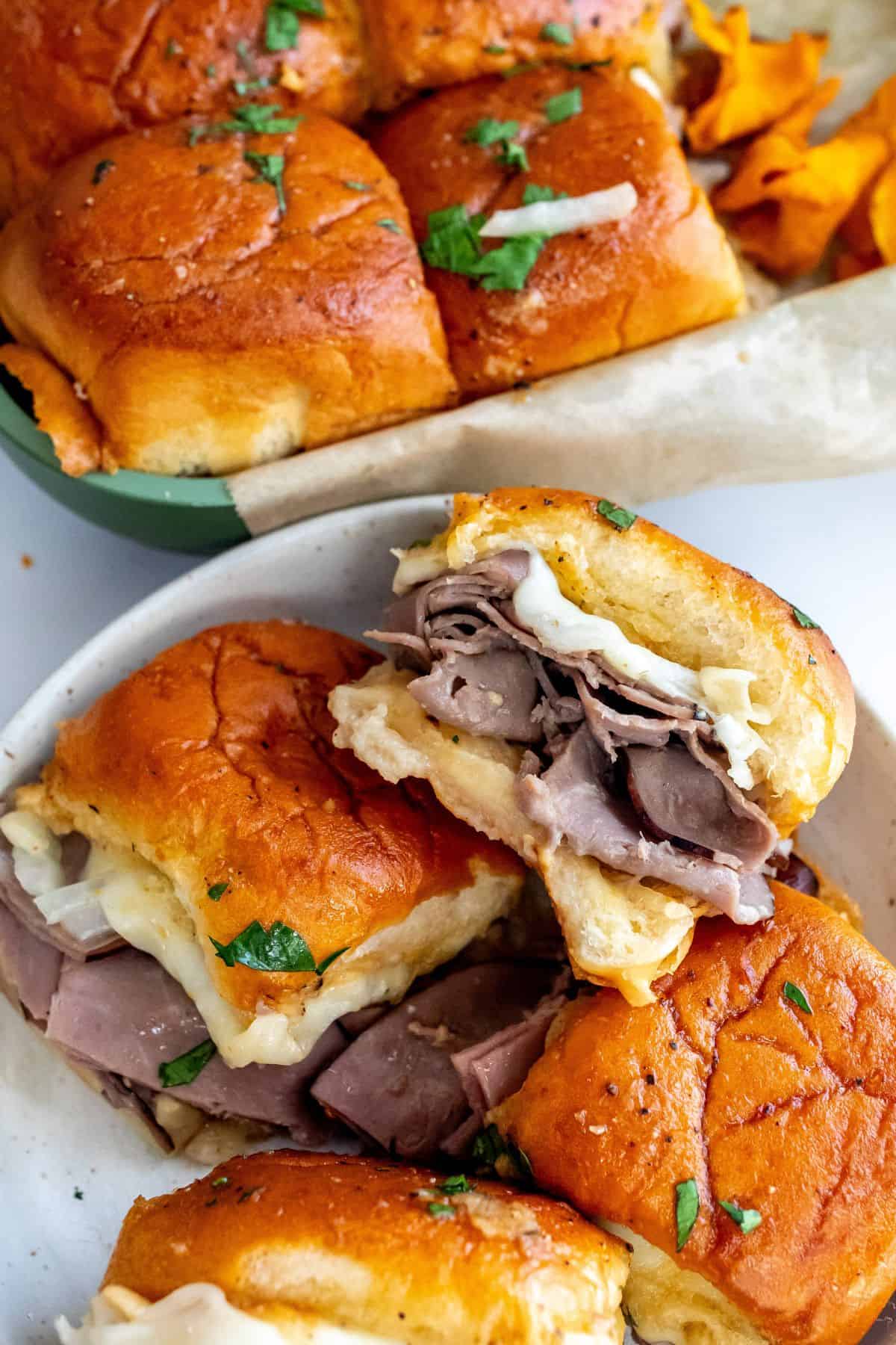 Up close photo of roast beef sliders on a plate with cheese and parsley. 