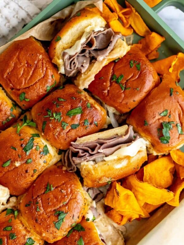 Roast beef sliders in a green pan with sweet potato chips on the side.