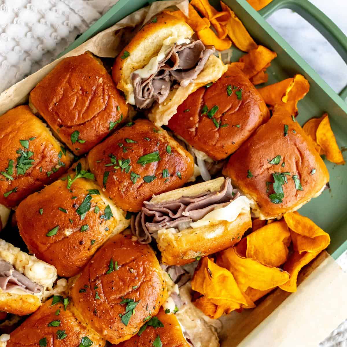 Roast beef sliders in a green pan with sweet potato chips on the side.