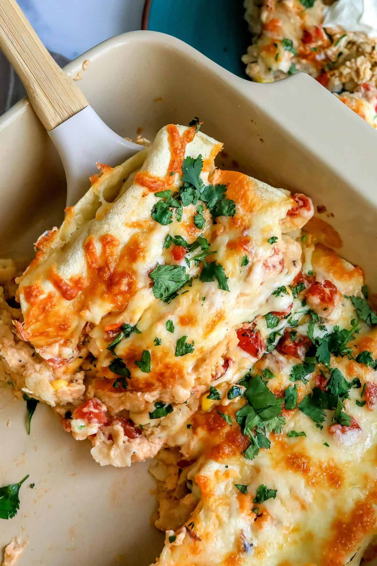 White Chicken Enchiladas up close in a baking dish with a spatula. 