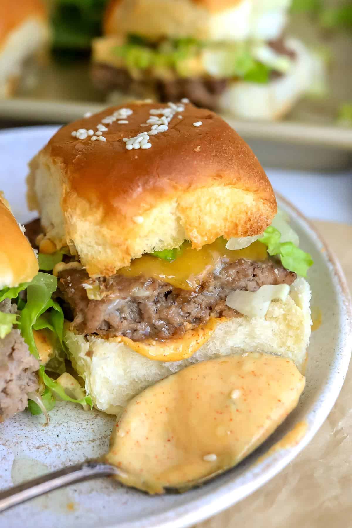 Up close photo of a big mac slider on a white plate with a saucy spoon. 