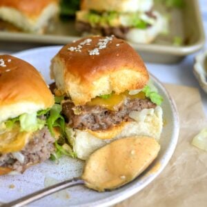 Up close photo of a big mac slider on a white plate with a saucy spoon.